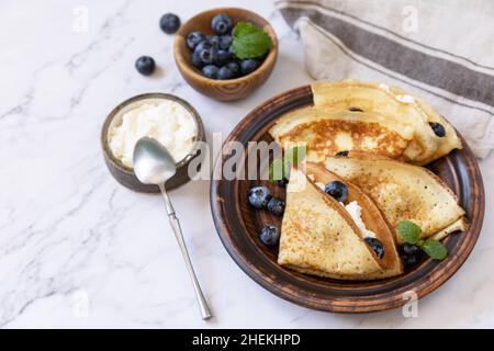 Wir feiern den Pfannkuchen-Tag, ein gesundes Frühstück. Köstliche hausgemachte Crepes mit Heidelbeeren und Ricota auf einer Steinplatte. Speicherplatz kopieren. Stockfoto