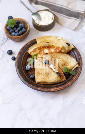 Wir feiern den Pfannkuchen-Tag, ein gesundes Frühstück. Köstliche hausgemachte Crepes mit Heidelbeeren und Riccota auf einer Steinplatte. Speicherplatz kopieren. Stockfoto