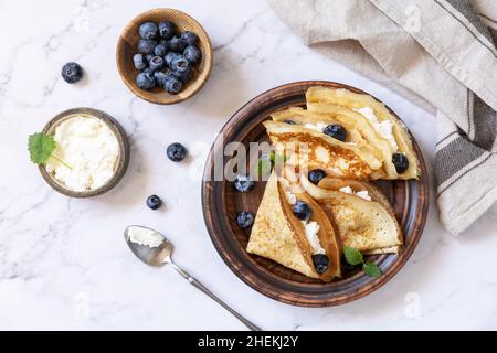 Wir feiern den Pfannkuchen-Tag, ein gesundes Frühstück. Köstliche hausgemachte Crepes mit Heidelbeeren und Ricota auf einer Steinplatte. Draufsicht flach liegend. Stockfoto