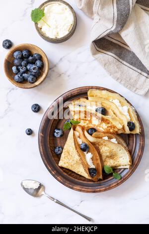 Wir feiern den Pfannkuchen-Tag, ein gesundes Frühstück. Köstliche hausgemachte Crepes mit Heidelbeeren und Ricota auf einer Steinplatte. Draufsicht flach liegend. Stockfoto