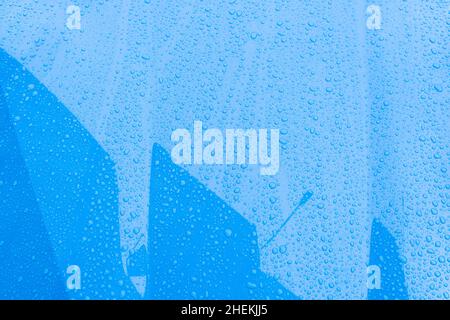 Blaue Autooberfläche mit Wassertropfen. Nahaufnahme Wassertropfen mit Gebäude Reflexion an Herbst regnerischen Tagen. Regen nasses Wetter Hintergrund Stockfoto
