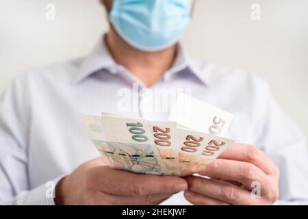Zählen kleine Geldscheine der Tschechischen Republik Koruna. Finanzierung während des Coronavirus in Tschechien Konzept. CZK kleine Banknoten. Mann in einer schützenden Medica Stockfoto