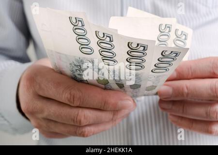 Finanzierung während des Coronavirus in Tschechien Konzept. Zählen Tschechische Krone CZK 5000 Banknoten. Mann in einer schützenden medizinischen Gesichtsmaske Atemschutzmaske hält krona Stockfoto