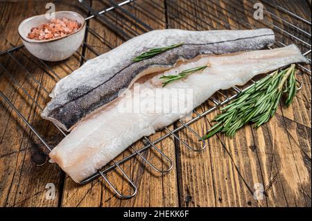 Rohe Fischfilets auf Grill mit Rosmarin und Kräutern. Holzhintergrund. Draufsicht Stockfoto