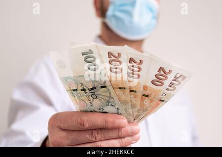 Fan von Cash Tschechische republik Krone. Finanzierung während des Coronavirus in Tschechien Konzept. CZK kleine Banknoten. Mann in einer schützenden medizinischen Gesichtsmaske hält kro fest Stockfoto