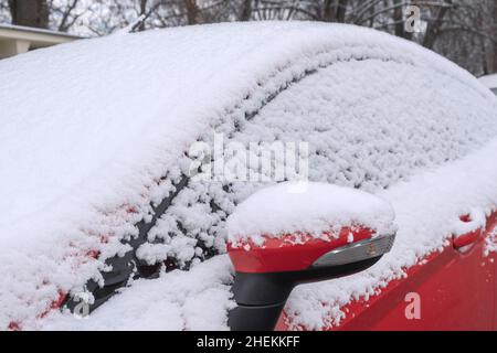 Rotes Auto bedeckt mit Schnee auf der Straße. An einem Wintermorgen. Transport im schneereichen kalten Winter Stockfoto