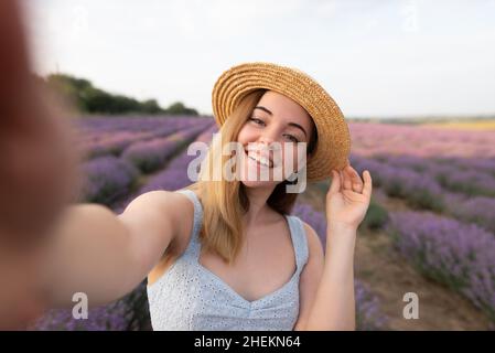 Im Freien romantisches Porträt von jungen glücklichen und attraktiven Frau in weißen Sommerkleid Selfie mit Handy auf schönen Lavendelblüten Stockfoto