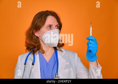Arzt in weißer Uniform mit einem Quecksilberthermometer in der Hand auf rotem Hintergrund Stockfoto