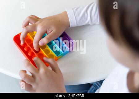 Mädchen Hände close up spielen mit rainbow Pop es fidget. Das Konzept der psychischen Gesundheit popit Spielzeug Stockfoto