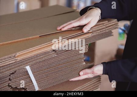 Frau nimmt gefaltete Stapel von Wellpappe zum Verpacken im Lager, Stapel von Wellpappenblättern und gebrauchsfertig Stockfoto