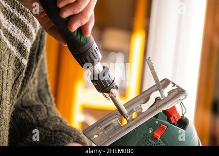 Manuelles Holzkonzept. Beschnittenes Nahaufnahme Foto des Handwerkers des Tischlerhandwerks mit Elektrowerkzeug in den Händen machen Möbel in der Garage oder im Arbeitsraum Stockfoto