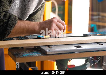 Selbstbewusster Experte für Holzarbeiter. Junger Mann, der in der Fabrik arbeitet. Gelernter Schreiner, der in seiner Holzwerkstatt ein Stück Holz schneidet. Stockfoto