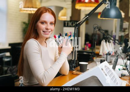 Porträt von lächelnden ziemlich junge Frau Client zeigt Farbe von bunten Nägeln Tipps in Maniküre Salon. Stockfoto