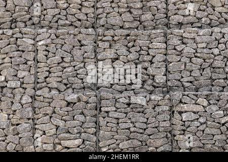 Gabionenstruktur, Hintergrundstruktur. Käfigkästen gefüllt mit Steinen für den Einsatz im Tiefbau, Straßenbau, militärische Anwendungen und Landschaftsbau Stockfoto