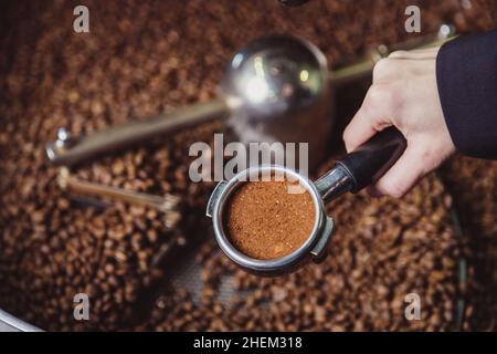 Nahaufnahme Mädchen Hand hält einen Portafilter mit gemahlenem Kaffee. Der Barista hält einen Portafilter und einen Kaffeemanipulationsfilter, der einen Espresso zubereitet. Stockfoto