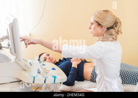 Schöne Gynäkologin untersucht die medizinischen Geräte. Der Patient liegt auf dem Tisch Stockfoto