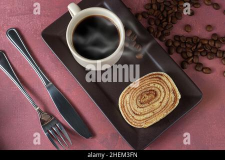 Scheibe Bolo de rolo (Kuchenrolle) neben Besteck, Tasse und Kaffeebohnen. Stockfoto