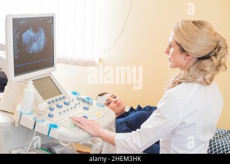 Schöne Gynäkologin untersucht die medizinischen Geräte. Der Patient liegt auf dem Tisch Stockfoto