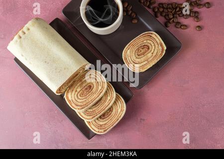 In Scheiben geschnittener Bolo de rolo (Rollkuchen) neben Tasse und Kaffeebohnen. Stockfoto