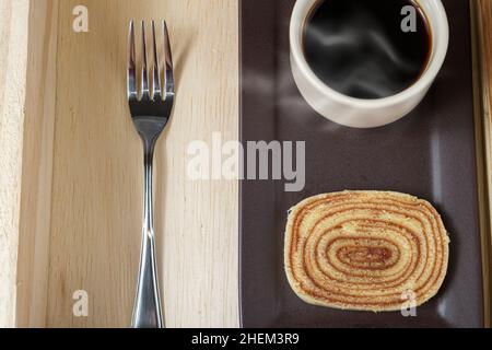 Nahaufnahme einer Scheibe bolo de rolo auf einem braunen Teller, neben einer Tasse Kaffee und einer Gabel. Stockfoto