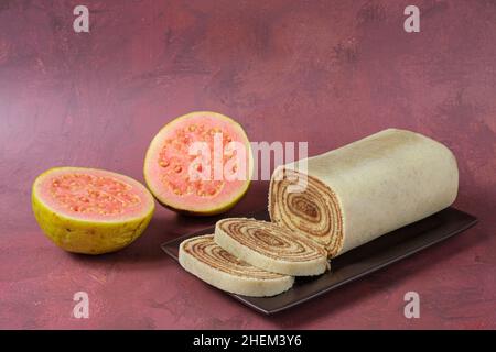 Bolo de rolo in Scheiben geschnitten auf einem braunen Teller, neben einer Guave. Stockfoto