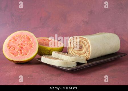 Bolo de rolo in Scheiben geschnitten auf einer braunen Platte, neben einer Guave (Seitenansicht). Stockfoto