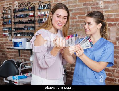 Lächelnde Frau Client suchen Farbe von Nagellack mit Manikuristin Stockfoto