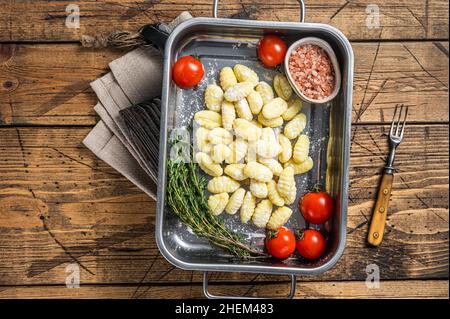 Ungekochte Gnocchi aus roher Kartoffel in Küchenblech mit Kräutern. Holzhintergrund. Draufsicht Stockfoto
