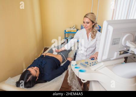 Schöne Gynäkologin untersucht die medizinischen Geräte. Der Patient liegt auf dem Tisch Stockfoto