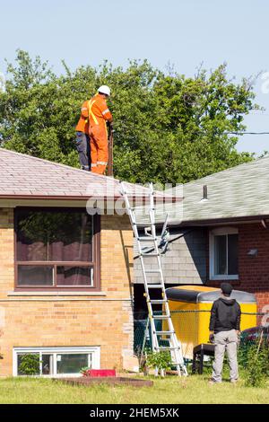 Toronto, Kanada, 2015: Arbeiter befestigen elektrische Drähte an einem Mast auf einem Haus. Stockfoto