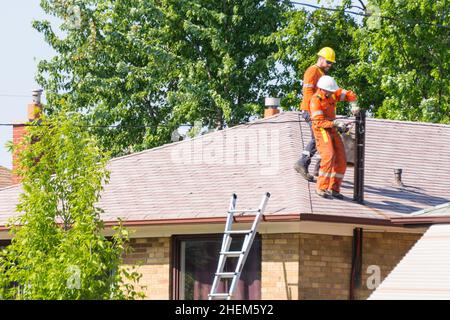 Toronto, Kanada, 2015: Arbeiter befestigen elektrische Drähte an einem Mast auf einem Haus. Stockfoto