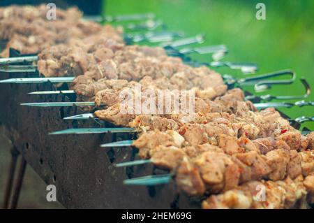 Grillkochen auf dem Grill wird das Fleisch auf den Spiessen in einer Reihe gestapelt. Duftender Rauch. Stockfoto