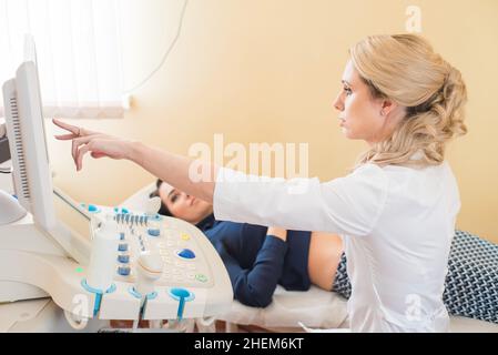 Schöne Gynäkologin untersucht die medizinischen Geräte. Der Patient liegt auf dem Tisch Stockfoto