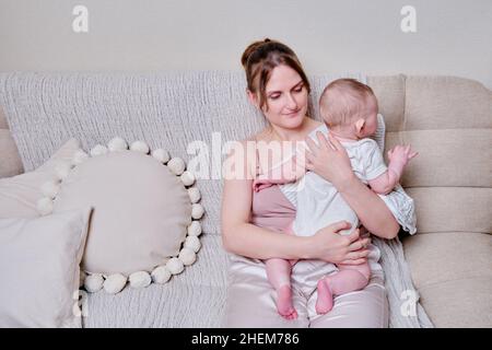 Eine Mutter hält ein Kleinkind, um überschüssige Luft nach dem Stillen wieder aufzublasen. Mama mit einem Jungen hält sich nach dem Füttern senkrecht Stockfoto