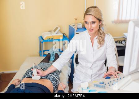 Schöne Gynäkologin untersucht die medizinischen Geräte. Der Patient liegt auf dem Tisch Stockfoto