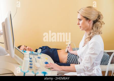 Schöne Gynäkologin untersucht die medizinischen Geräte. Der Patient liegt auf dem Tisch Stockfoto