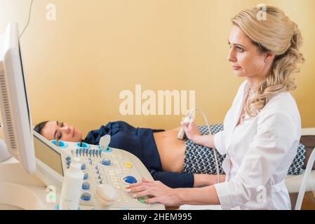 Schöne Gynäkologin untersucht die medizinischen Geräte. Der Patient liegt auf dem Tisch Stockfoto