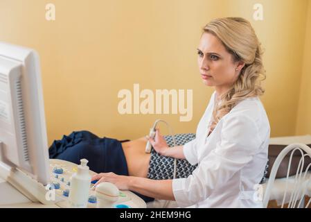 Schöne Gynäkologin untersucht die medizinischen Geräte. Der Patient liegt auf dem Tisch Stockfoto