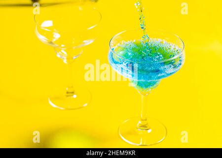 Barkeeper gießt Blue Lagoon curacao Sirup mit Wodka und Limonade Cocktail aus einem Shaker in ein Glas Alkohol auf einem leuchtend gelben Backgrou gemischt Stockfoto