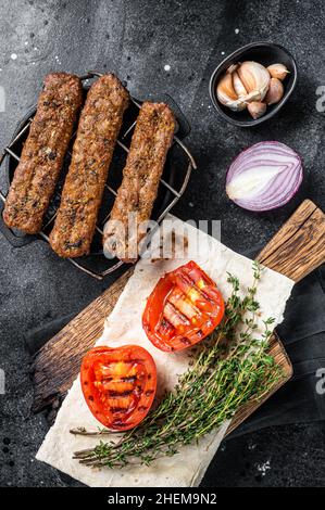 BBQ adana Shish Kebab auf einem Grill mit Brot und Tomaten. Schwarzer Hintergrund. Draufsicht Stockfoto