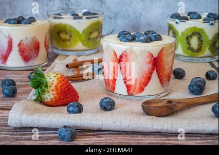 Hausgemachtes gesundes Frühstück in einem Glas mit frischen Früchten: Kiwi, Erdbeere und Joghurt auf Holzgrund. Geringe Schärfentiefe mit selektivem FOC Stockfoto