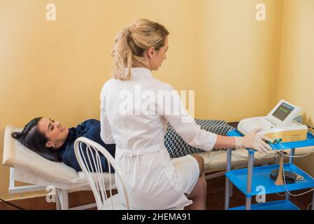 Schöne Gynäkologin untersucht die medizinischen Geräte. Der Patient liegt auf dem Tisch Stockfoto