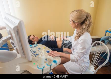 Schöne Gynäkologin untersucht die medizinischen Geräte. Der Patient liegt auf dem Tisch Stockfoto