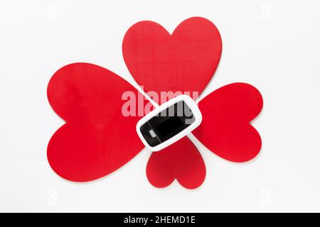 Covid Valentinstag Geschenk-Konzept, Pulsoximeter zwischen Blume aus roten Herzen auf weißem Hintergrund Draufsicht Stockfoto