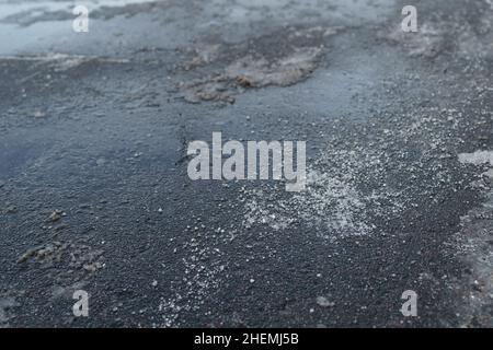 Enteisungsreagenz im Winter auf der Straße. Der Bürgersteig ist mit technischem Salz bestreut Stockfoto