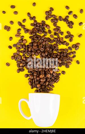 Kaffeebohnen kommen aus einer Tasse vor einem gelben Hintergrund Stockfoto