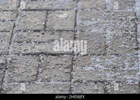 Enteisungsreagenz im Winter auf der Straße. Der Bürgersteig ist mit technischem Salz bestreut Stockfoto