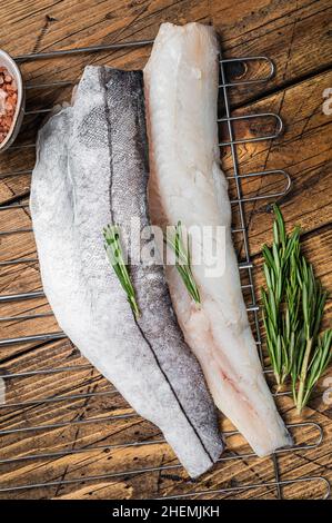 Rohe Fischfilets auf Grill mit Rosmarin und Kräutern. Holzhintergrund. Draufsicht Stockfoto