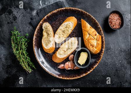 Knoblauch auf geröstetem Baguette mit Salz, Pfeffer, Thymian und Olivenöl auf dem Teller verteilen. Schwarzer Hintergrund. Draufsicht Stockfoto