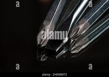 Nahaufnahme aus einer Sammlung von flachen und kreuzenden Metallschraubern auf schwarzem Hintergrund Stockfoto